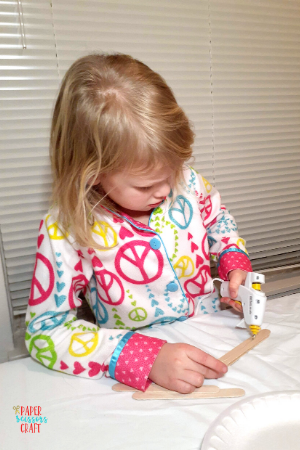 Little girl using a low temperature glue gun to put glue on a popsicle stick.