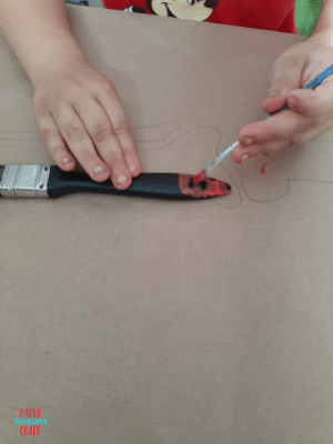 Painting a black paintbrush handle with red paint.