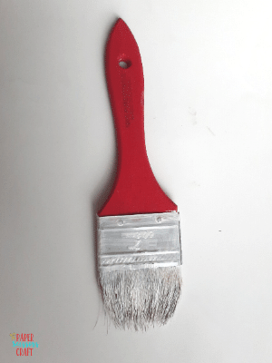 Paintbrush with a red handle and bristles painted white.