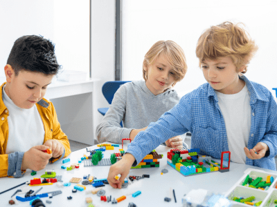 Three boys sitting at a table and playing with Legos.