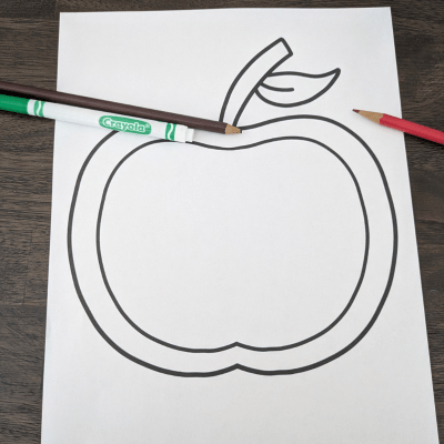 Apple template on white paper with a green marker, brown colored pencil, and a pencil laying on top.