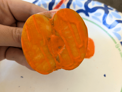 Half of an apple covered in orange paint on one side.