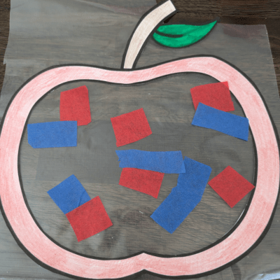 Apple template after being cut out and colored in on top of contact paper. with red and blue tissue paper square on top.