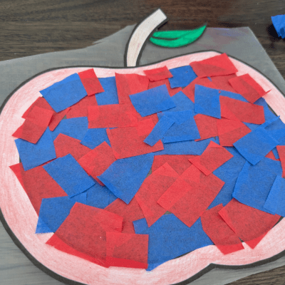 Apple template after being cut out and colored in on top of contact paper completely filled with red and blue tissue paper squares on top.