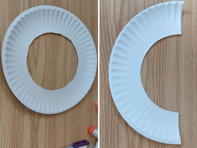 White paper plate with hole cut out of the middle and a paper plate cut into a crescent shape.