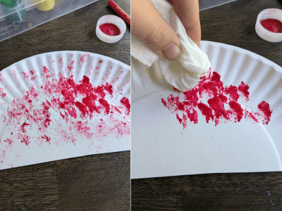 Sponge painting a paper plate with red paint.