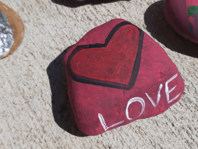 Flat rock that has been painted red with a heard and the word love in white.