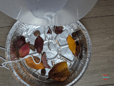 Water being poured into an aluminum pan with leaves inside of it.