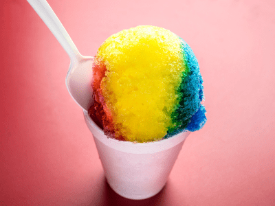 Rainbow snow cone with plastic spoon sticking out of it.