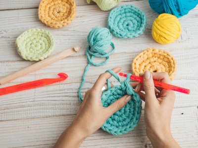 A person making a blue crochet item.