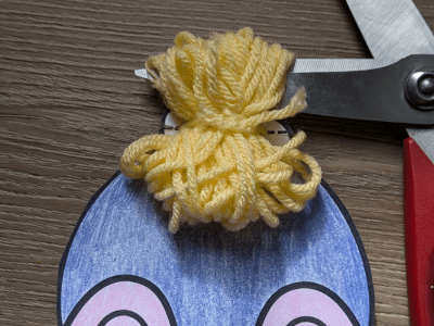 Yellow yarn pom-pom attached as a bunny tail to a paper bunny.